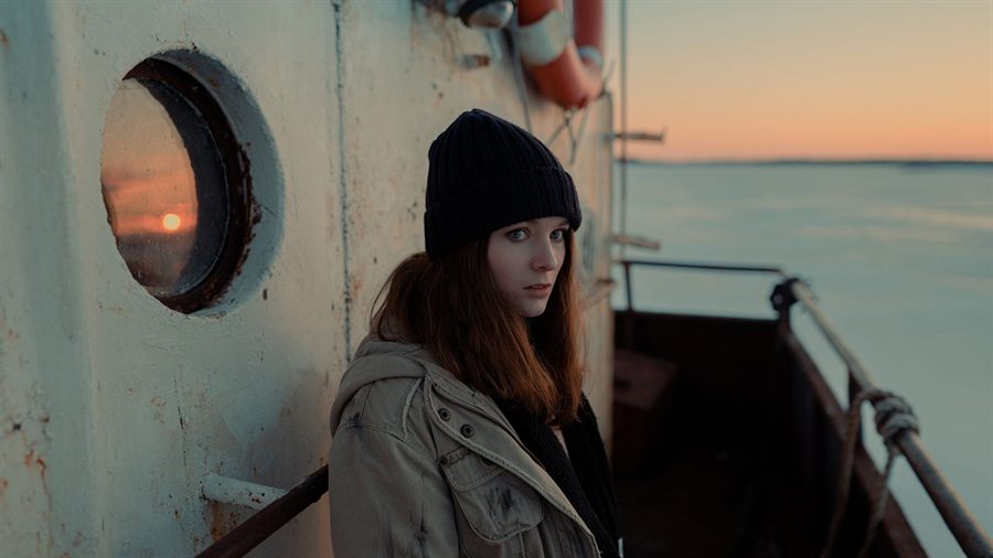 Traveler sitting by a porthole on a ship deck at sunset